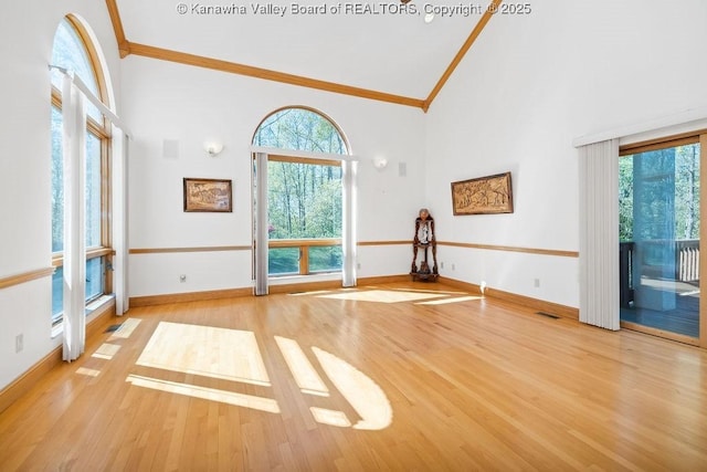 unfurnished living room with high vaulted ceiling, ornamental molding, light wood-type flooring, and baseboards