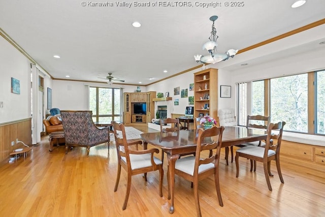 dining space with ornamental molding, a brick fireplace, wainscoting, and light wood-style flooring