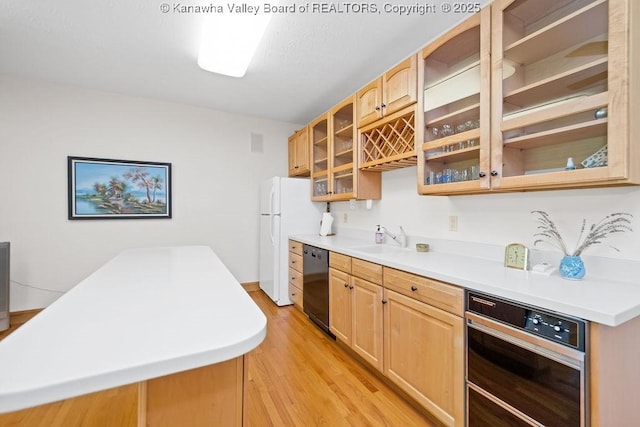 kitchen featuring light countertops, glass insert cabinets, wall oven, a sink, and dishwasher