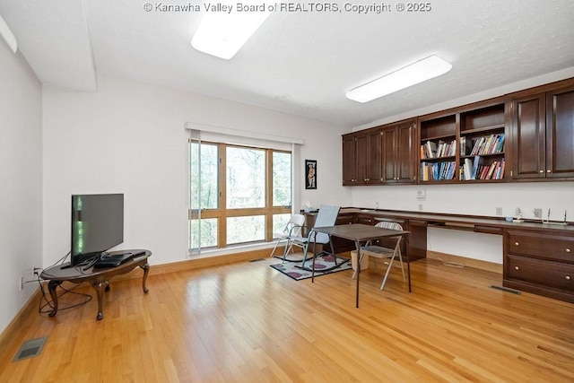 office space featuring baseboards, built in desk, visible vents, and light wood-style floors