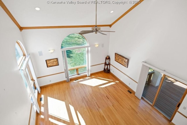 unfurnished living room with a towering ceiling, baseboards, ornamental molding, and wood finished floors