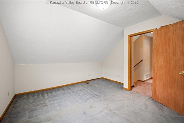 additional living space with a textured ceiling, lofted ceiling, light colored carpet, visible vents, and baseboards