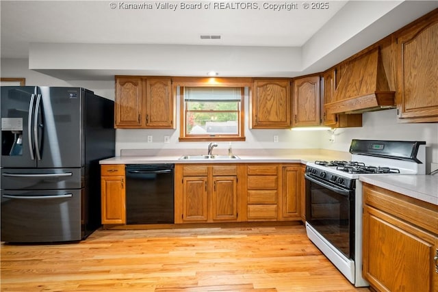 kitchen with a sink, light countertops, custom exhaust hood, black appliances, and brown cabinetry