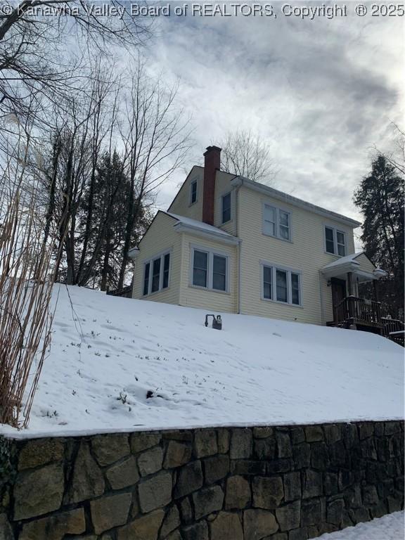 snow covered rear of property featuring a chimney