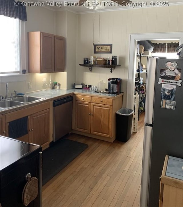 kitchen featuring a sink, light countertops, appliances with stainless steel finishes, light wood-type flooring, and brown cabinetry