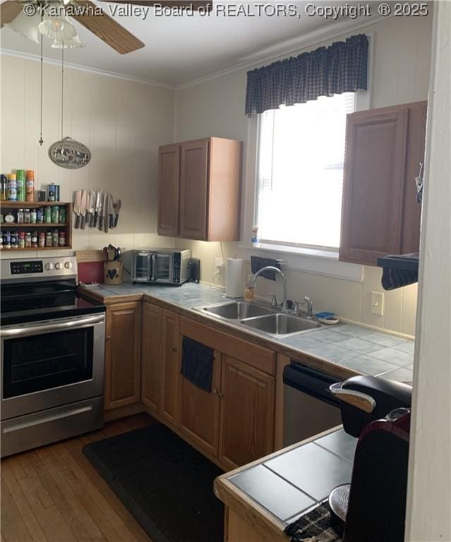 kitchen featuring tile countertops, stainless steel appliances, wood finished floors, a sink, and ornamental molding