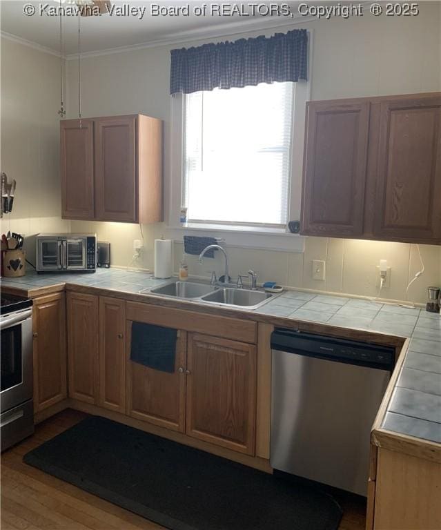 kitchen featuring tile countertops, appliances with stainless steel finishes, ornamental molding, a sink, and wood finished floors