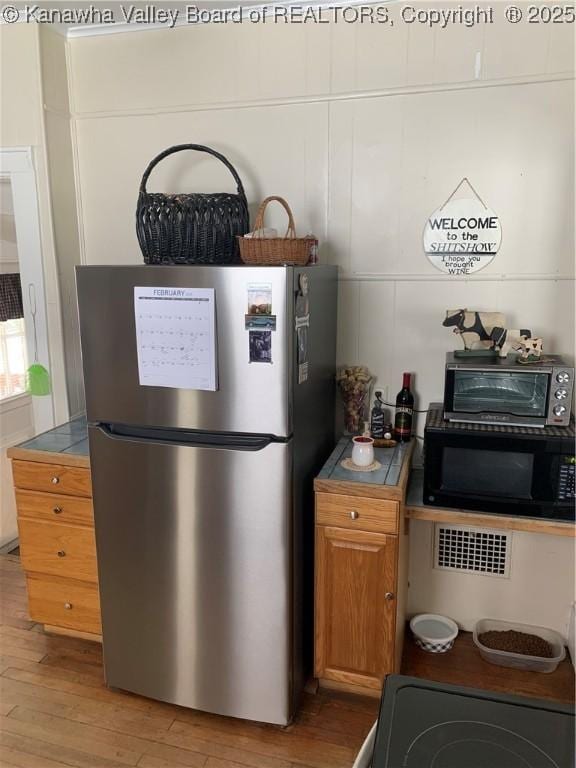 kitchen featuring a toaster, brown cabinets, freestanding refrigerator, light wood-type flooring, and black microwave