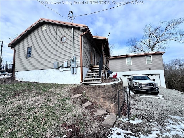 snow covered house featuring a garage, gravel driveway, and stairway