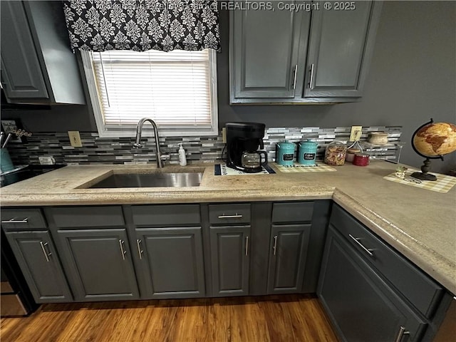 kitchen featuring gray cabinets, light countertops, backsplash, a sink, and wood finished floors