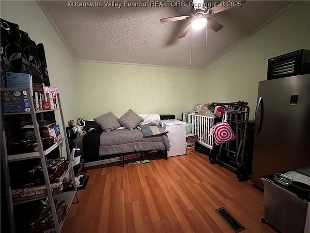 bedroom with visible vents, ornamental molding, wood finished floors, freestanding refrigerator, and a textured ceiling