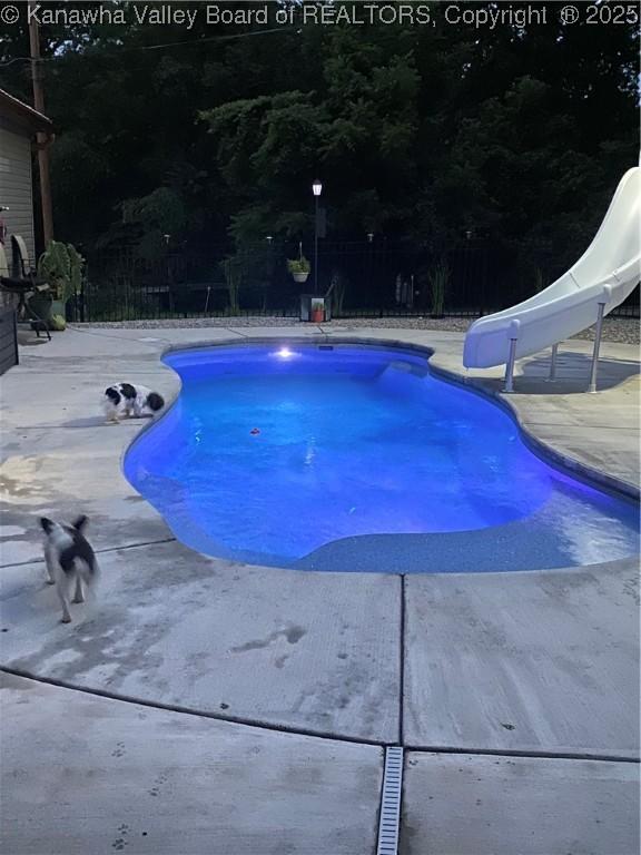 outdoor pool with a patio, a water slide, and fence