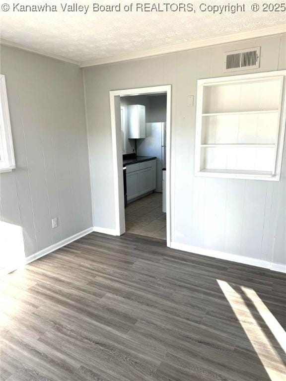 empty room with dark wood-style floors, visible vents, a textured ceiling, and ornamental molding