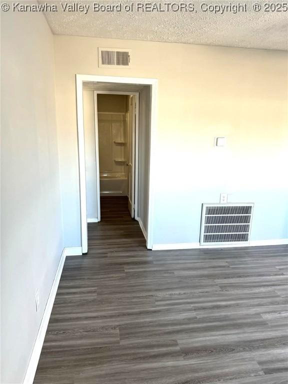 hall featuring visible vents, a textured ceiling, and dark wood-type flooring