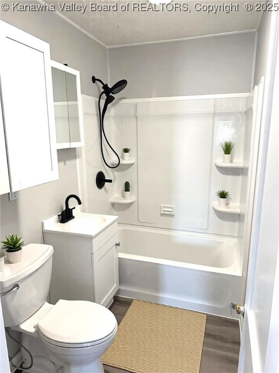 bathroom with vanity, washtub / shower combination, wood finished floors, a textured ceiling, and toilet