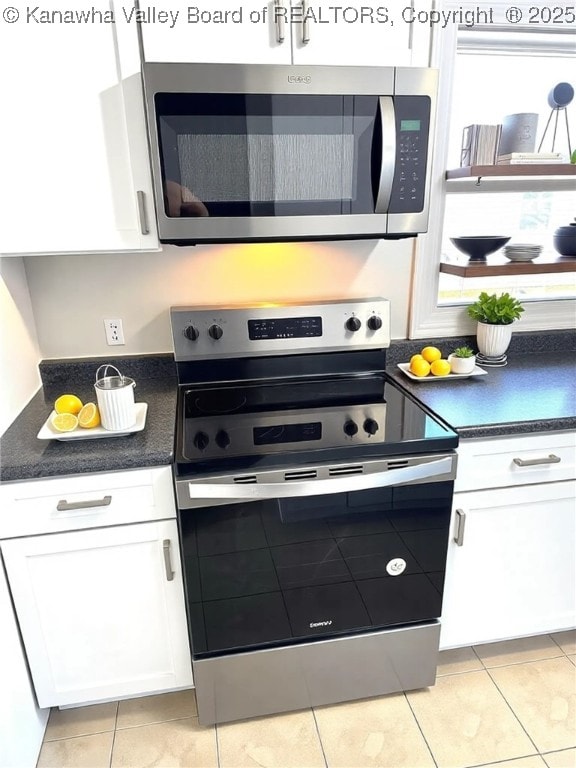 kitchen featuring white cabinetry, dark countertops, light tile patterned flooring, and stainless steel appliances