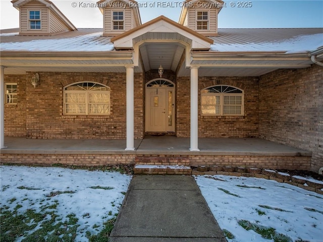 snow covered property entrance with covered porch and brick siding