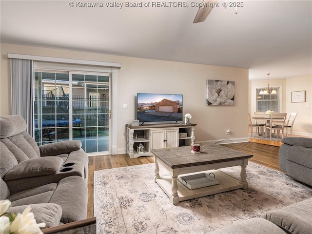 living area with light wood-type flooring, baseboards, and ceiling fan with notable chandelier