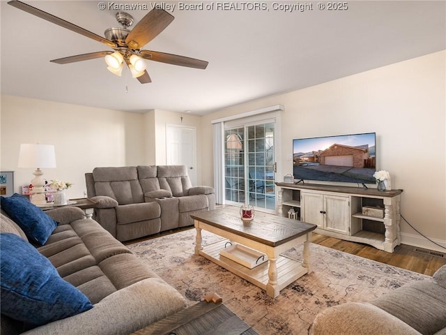 living room with dark wood-type flooring, visible vents, ceiling fan, and baseboards