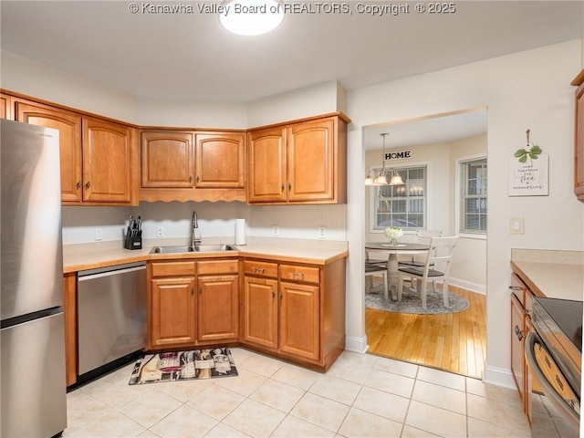 kitchen featuring decorative light fixtures, stainless steel appliances, light countertops, brown cabinetry, and a sink