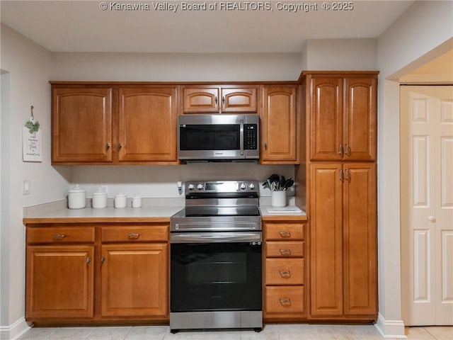 kitchen with stainless steel appliances, brown cabinetry, light countertops, and baseboards