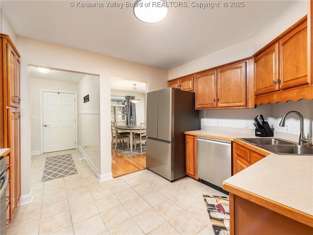 kitchen featuring brown cabinets, stainless steel appliances, a sink, and light countertops