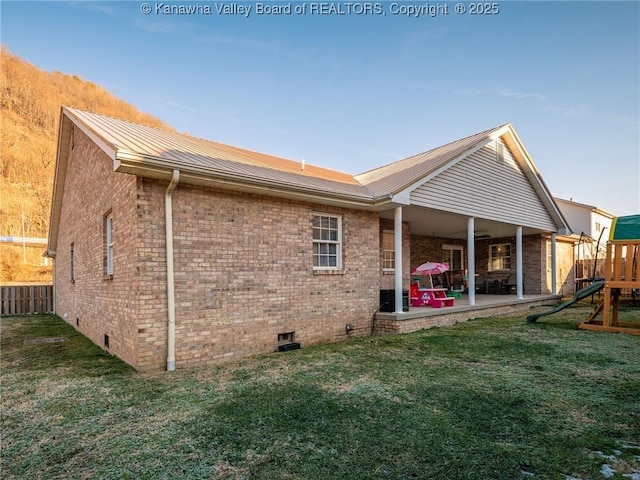 rear view of property featuring brick siding, crawl space, a playground, and a lawn