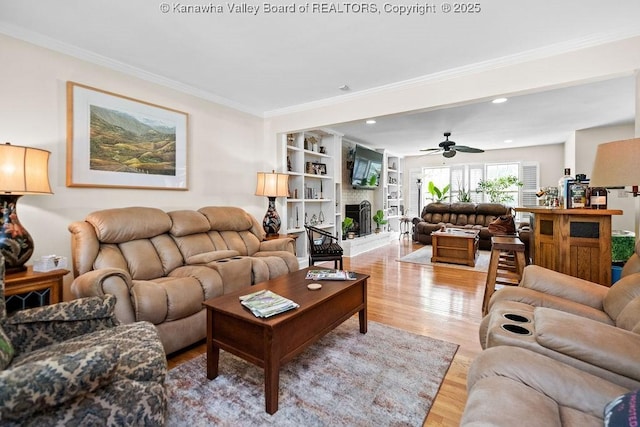 living room with crown molding, recessed lighting, light wood-style floors, a ceiling fan, and a large fireplace