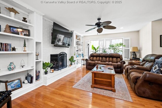 living area featuring built in shelves, light wood finished floors, a fireplace, and a ceiling fan