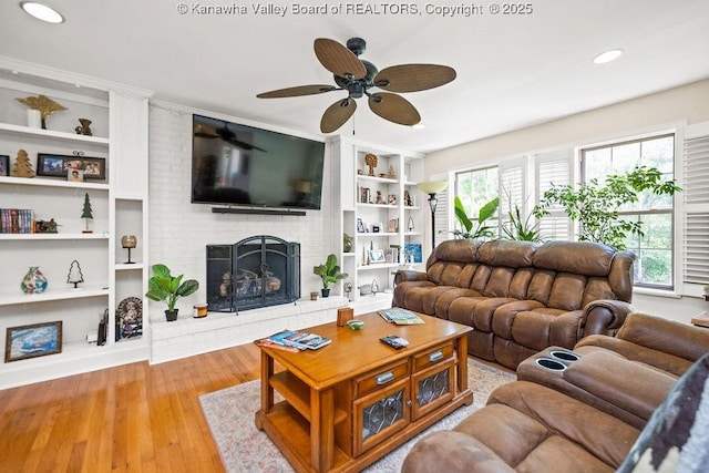 living area featuring a brick fireplace, ceiling fan, built in shelves, and wood finished floors