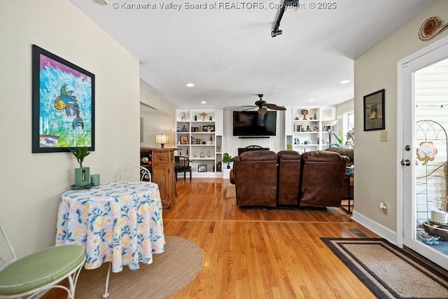 living area featuring built in shelves, light wood-type flooring, ceiling fan, and baseboards