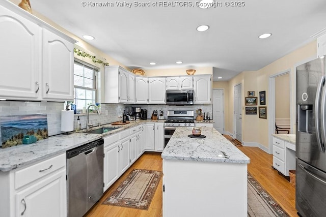 kitchen featuring appliances with stainless steel finishes, a sink, light wood finished floors, and a kitchen island