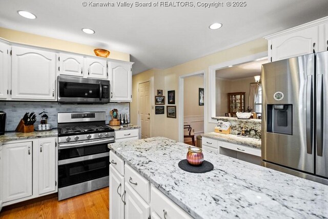 kitchen featuring light wood-type flooring, white cabinetry, stainless steel appliances, and decorative backsplash