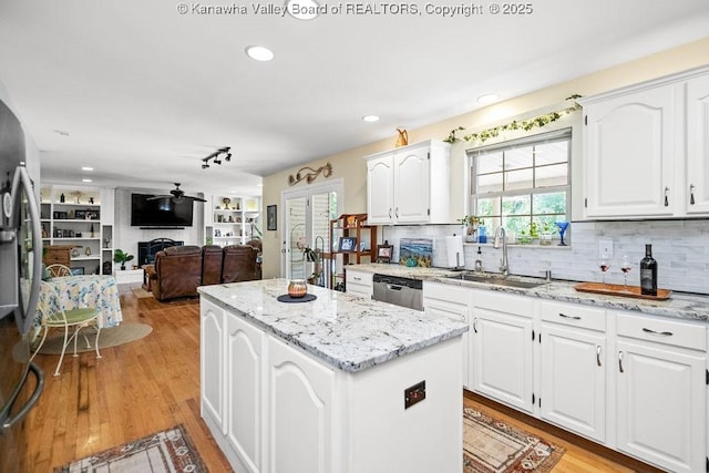 kitchen featuring light stone counters, a center island, stainless steel appliances, a fireplace, and a sink