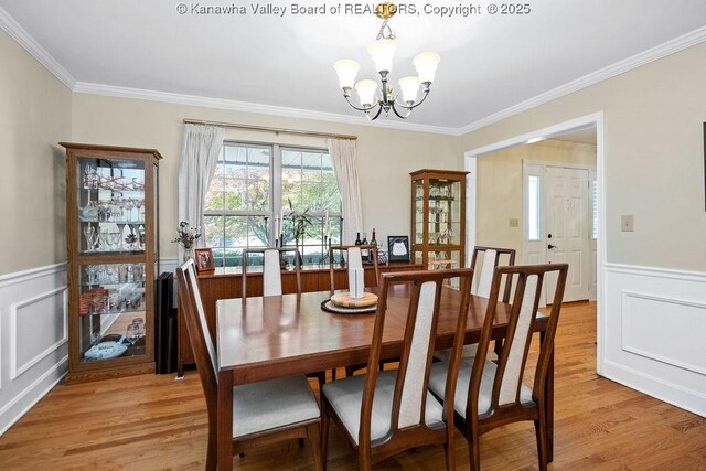 dining room with a chandelier, ornamental molding, a wainscoted wall, and light wood-type flooring