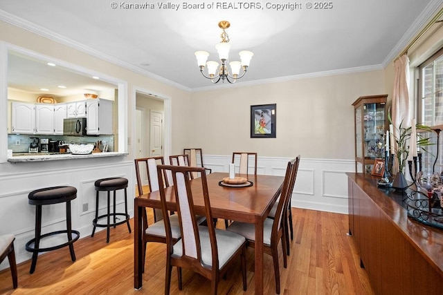 dining space with wainscoting, crown molding, light wood finished floors, and an inviting chandelier