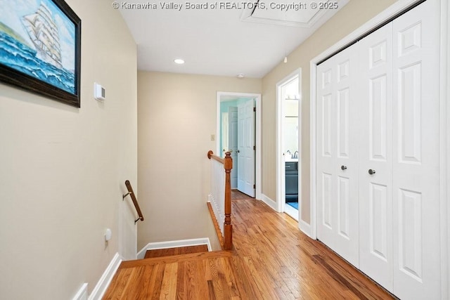 corridor featuring light wood-style floors, recessed lighting, baseboards, and an upstairs landing