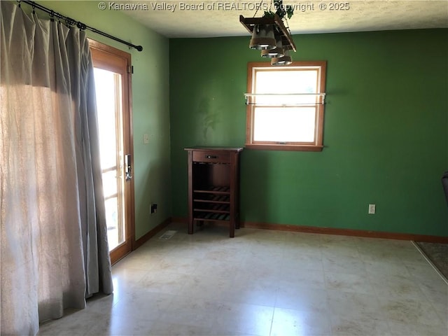 empty room with light floors, a healthy amount of sunlight, a textured ceiling, and baseboards