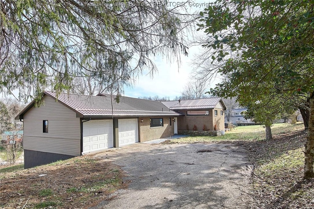 view of front of property featuring a garage, driveway, metal roof, and brick siding