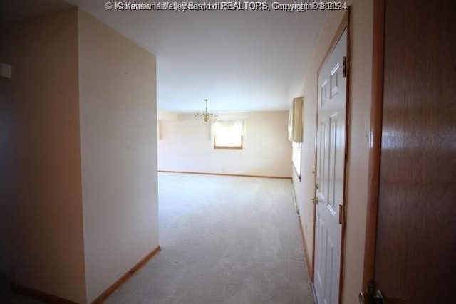 hall with light carpet, an inviting chandelier, and baseboards