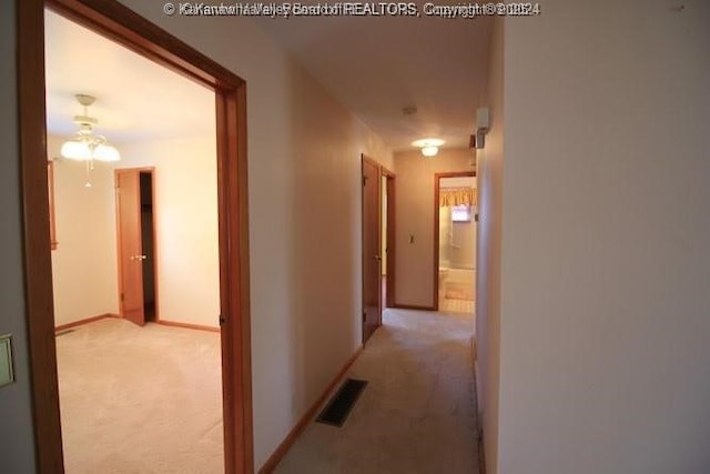 hall with light carpet, visible vents, and baseboards