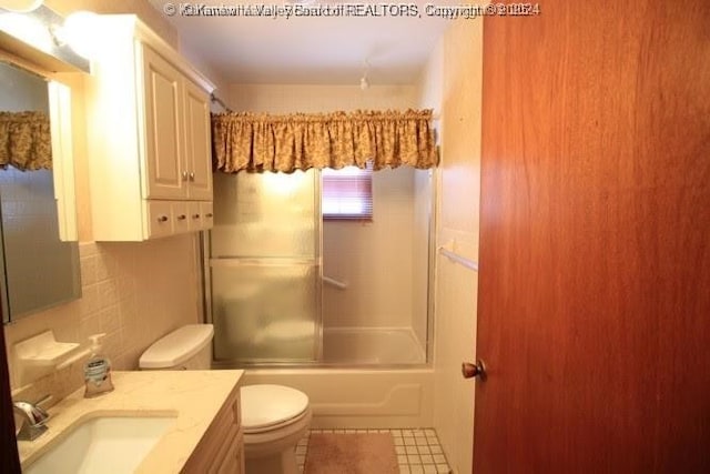 bathroom featuring toilet, shower / bath combination with glass door, vanity, tile walls, and tasteful backsplash