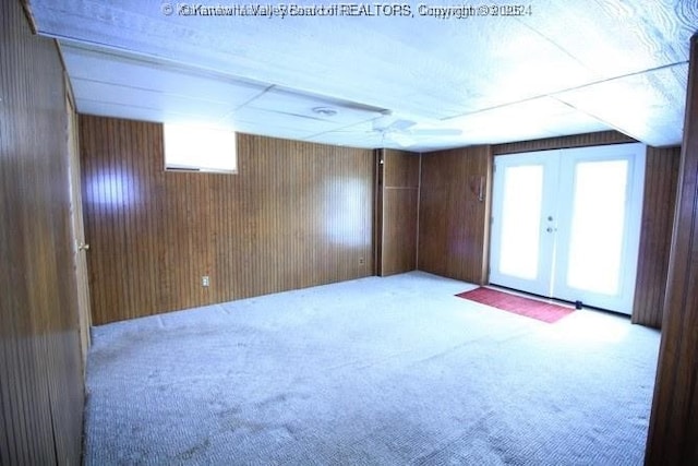 empty room featuring french doors, wood walls, and light colored carpet