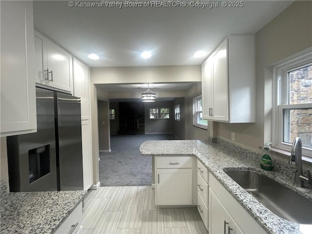 kitchen with pendant lighting, white cabinetry, a sink, light stone countertops, and stainless steel fridge with ice dispenser