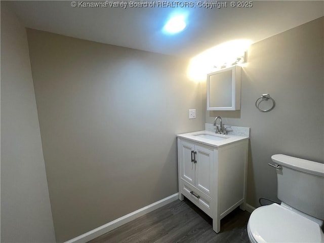 bathroom with toilet, wood finished floors, vanity, and baseboards