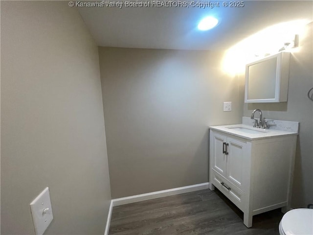 half bath featuring toilet, wood finished floors, vanity, and baseboards