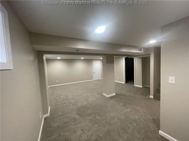 finished basement with baseboards, visible vents, and dark carpet