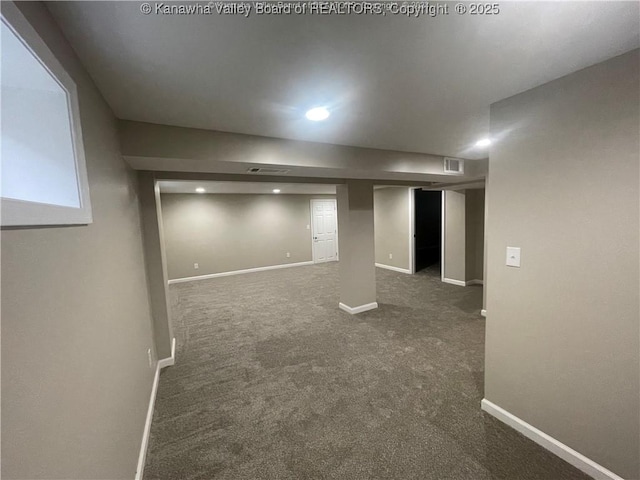 finished basement featuring visible vents, dark carpet, and baseboards