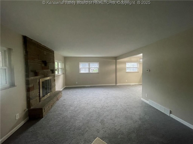 unfurnished living room with dark carpet, visible vents, a fireplace, and baseboards