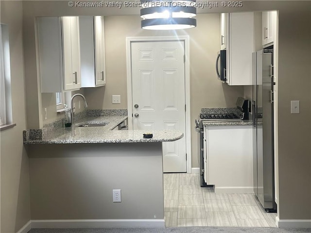 kitchen with appliances with stainless steel finishes, white cabinetry, a sink, and light stone counters